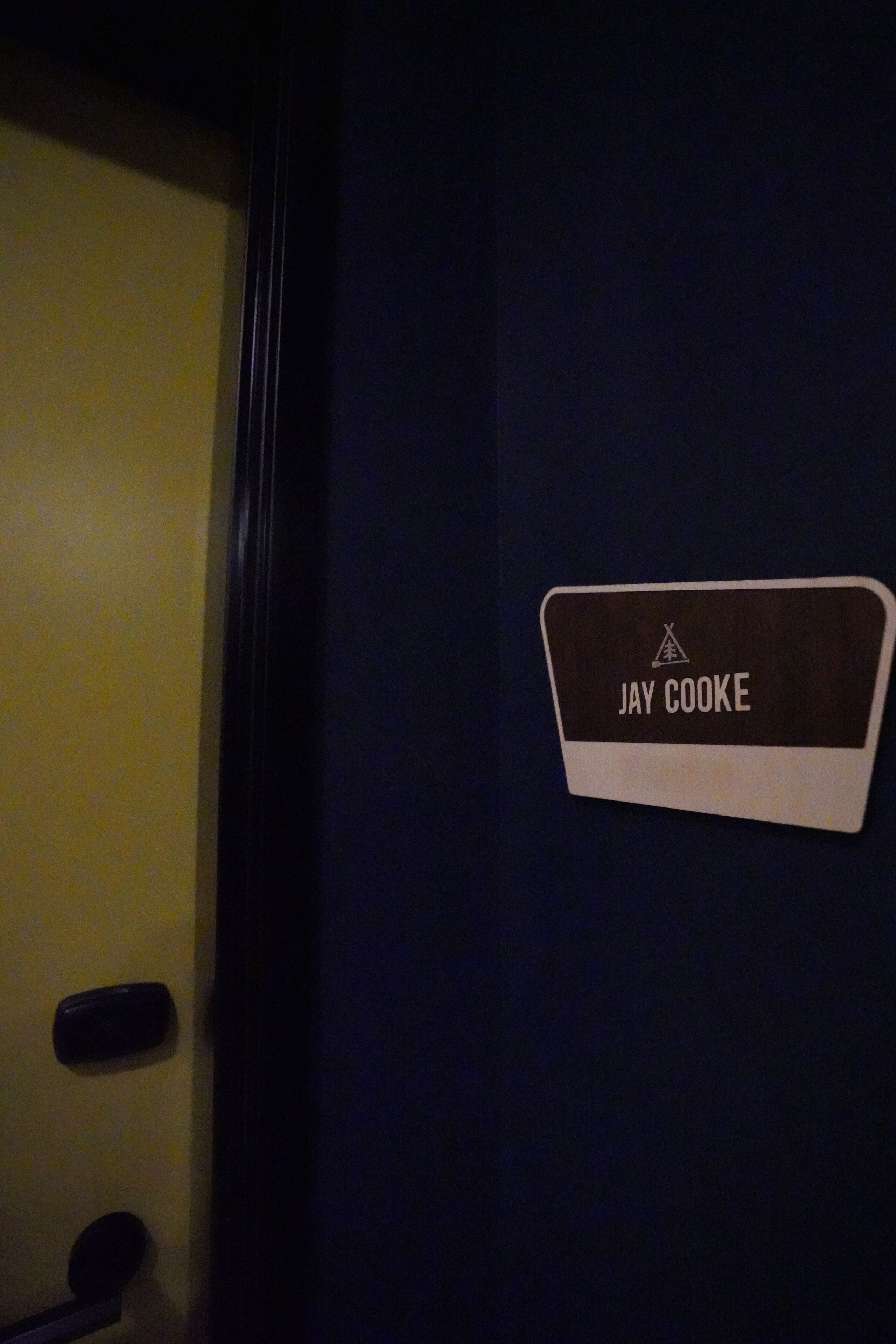 A nameplate on a wall with the name "JAY COOKE" and a logo above it.
