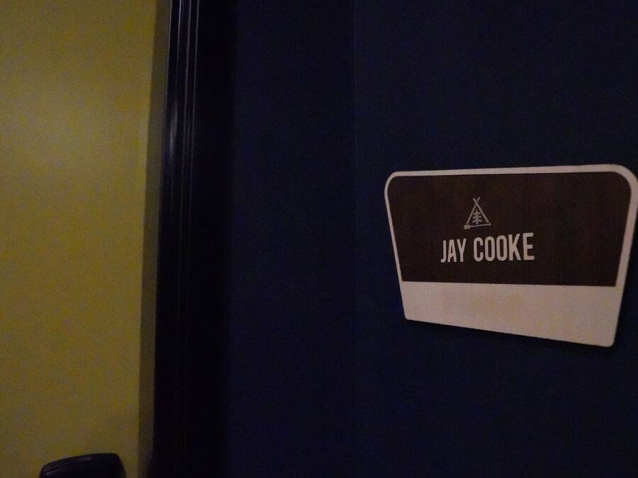 A nameplate on a wall with the name "JAY COOKE" and a logo above it.