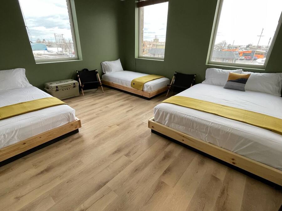 Una stanza con tre letti, ciascuno con struttura in legno e biancheria bianca, disposti a forma di U. Ampie finestre offrono vista all'esterno.