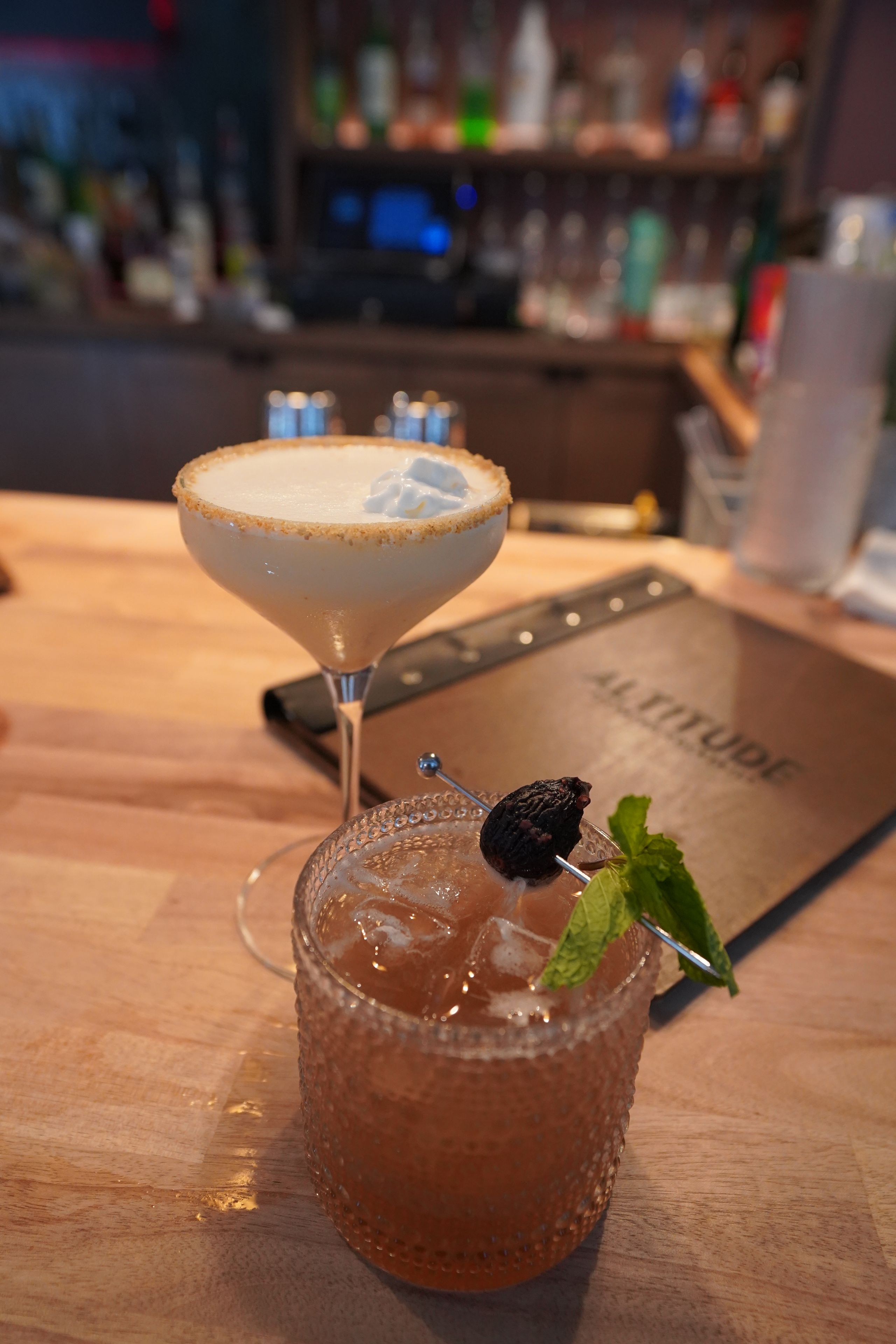 Un ambiente de bar con una copa de cóctel y una copa de martini sobre una superficie de madera.