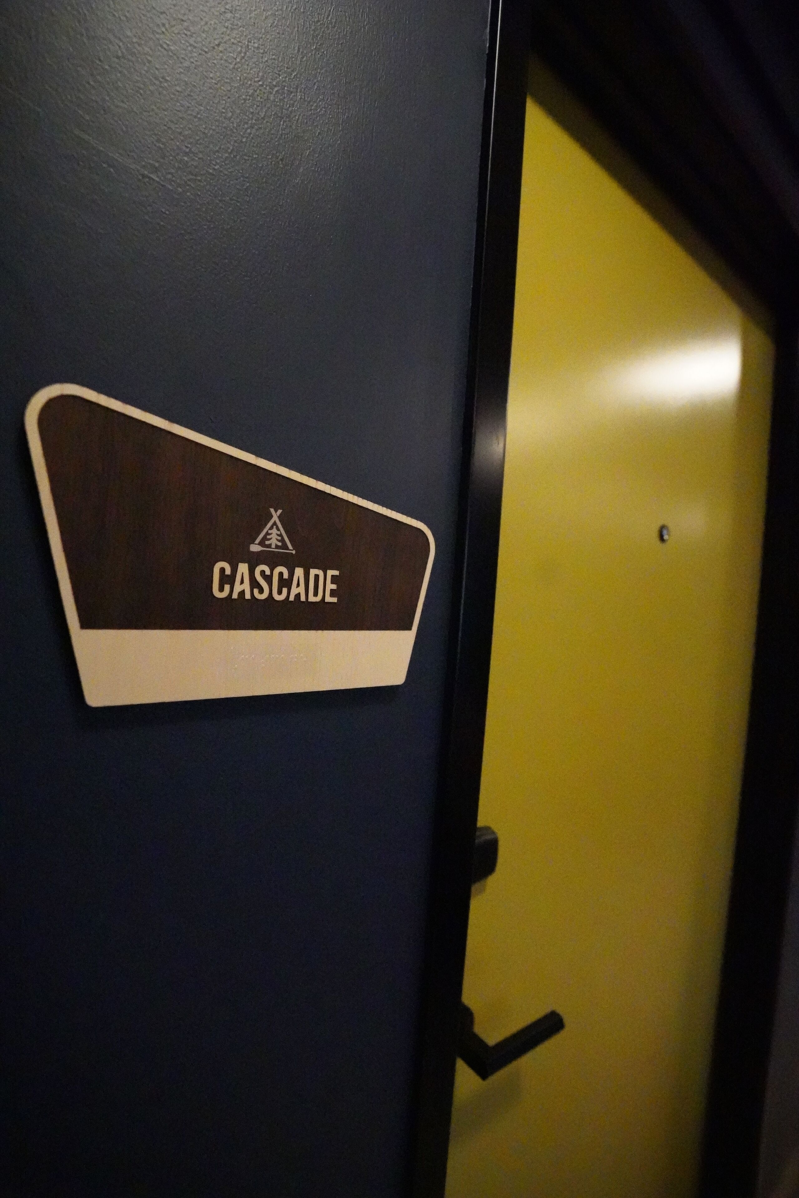 Een deur met een bordje met de tekst 'CASCADE' en een geel deurkozijn.