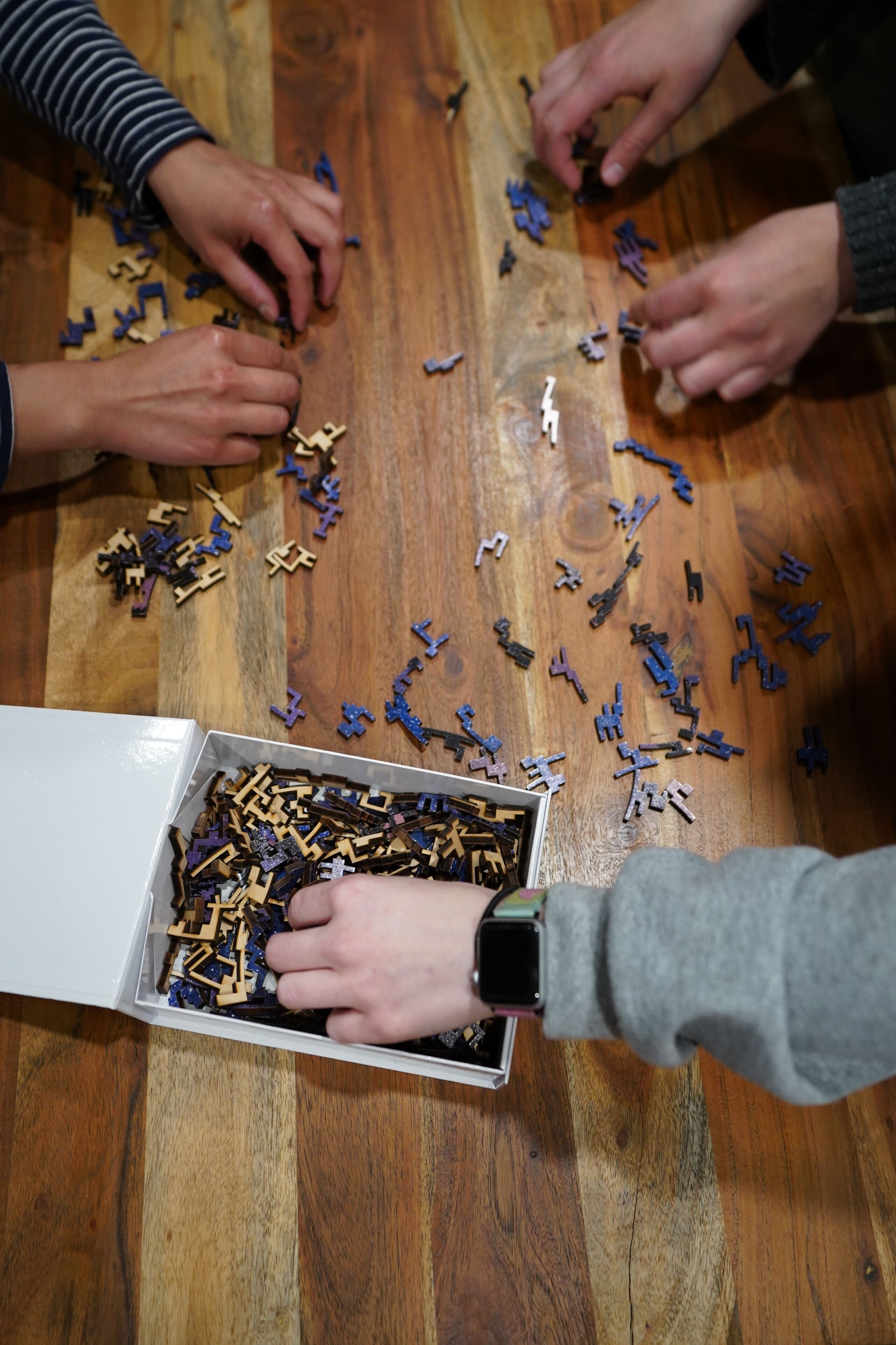 Un groupe de personnes est en train d’assembler des pièces de puzzle en bois sur une table en bois.