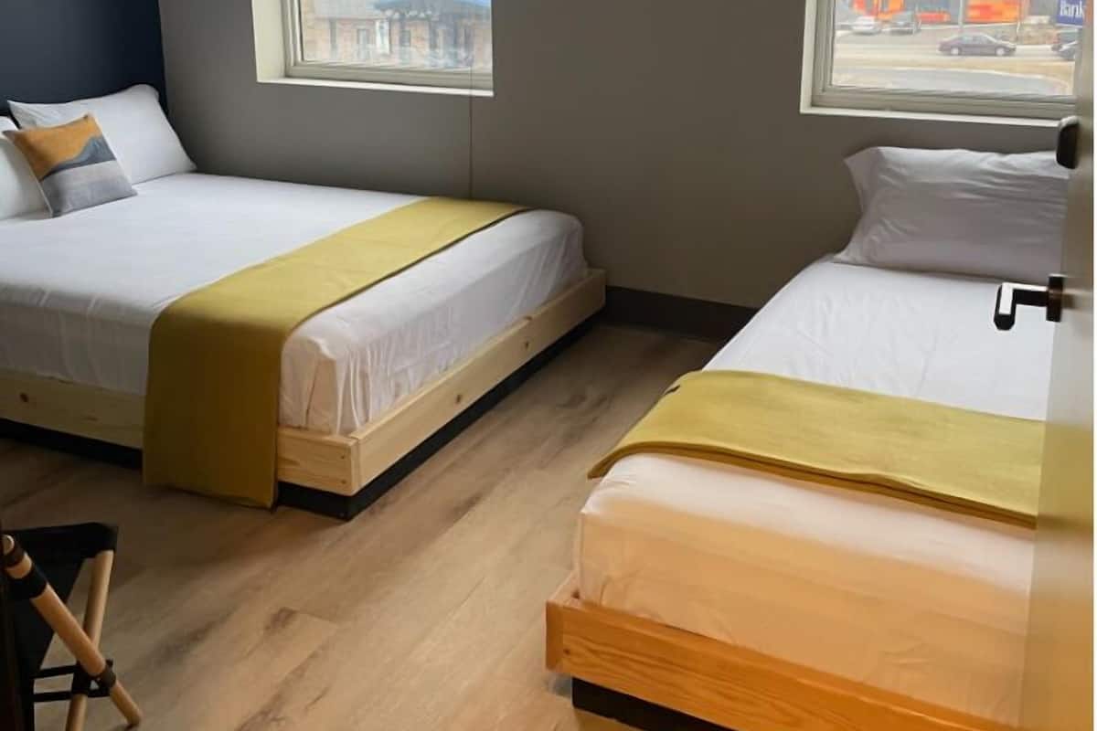 A hotel room with two single beds, wooden flooring, and a view of the street through the window.