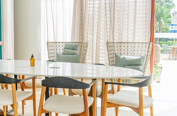 A dining area with a round table, chairs, wicker sofas, and a view of the outdoors.