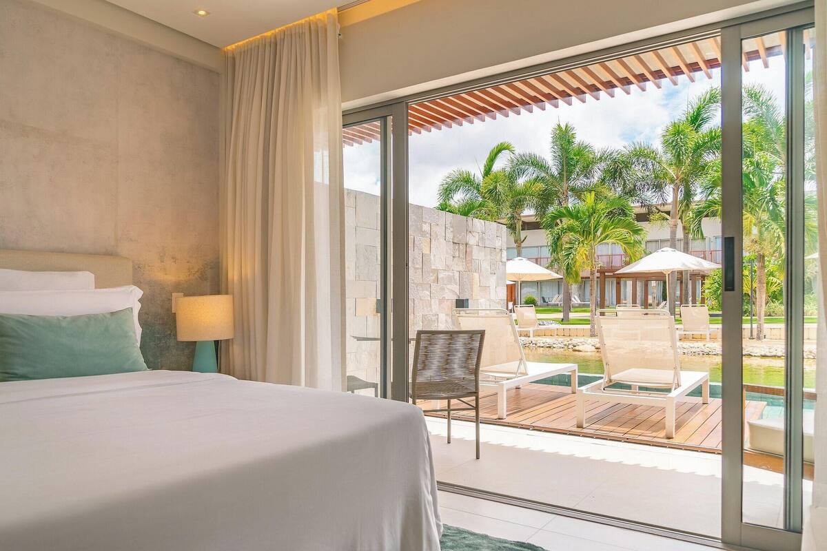 A hotel room with a large bed, a view of a pool area, and a stone wall.