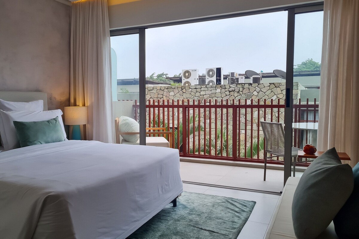 Une chambre d’hôtel comprenant un lit, une table de chevet, une lampe, une vue sur le balcon extérieur et un coin repas.