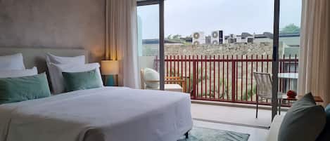 A hotel room with a bed, a nightstand, a lamp, a view of the outside balcony, and a dining area.