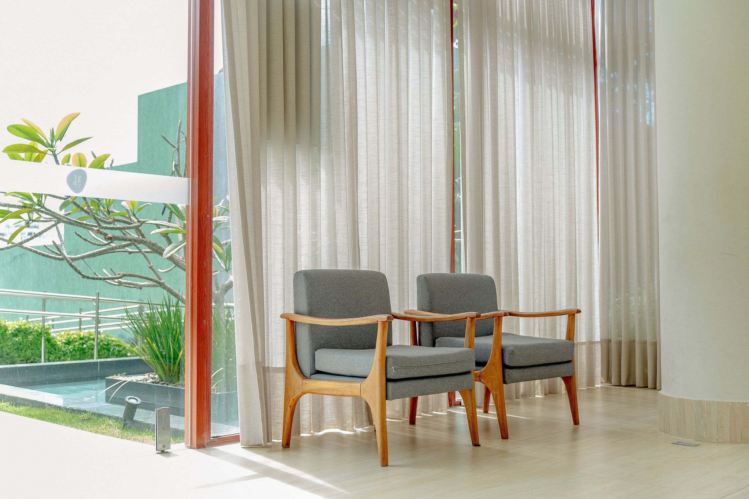 Two wooden-framed chairs with grey upholstery in a room with a large window and a view of a swimming pool.