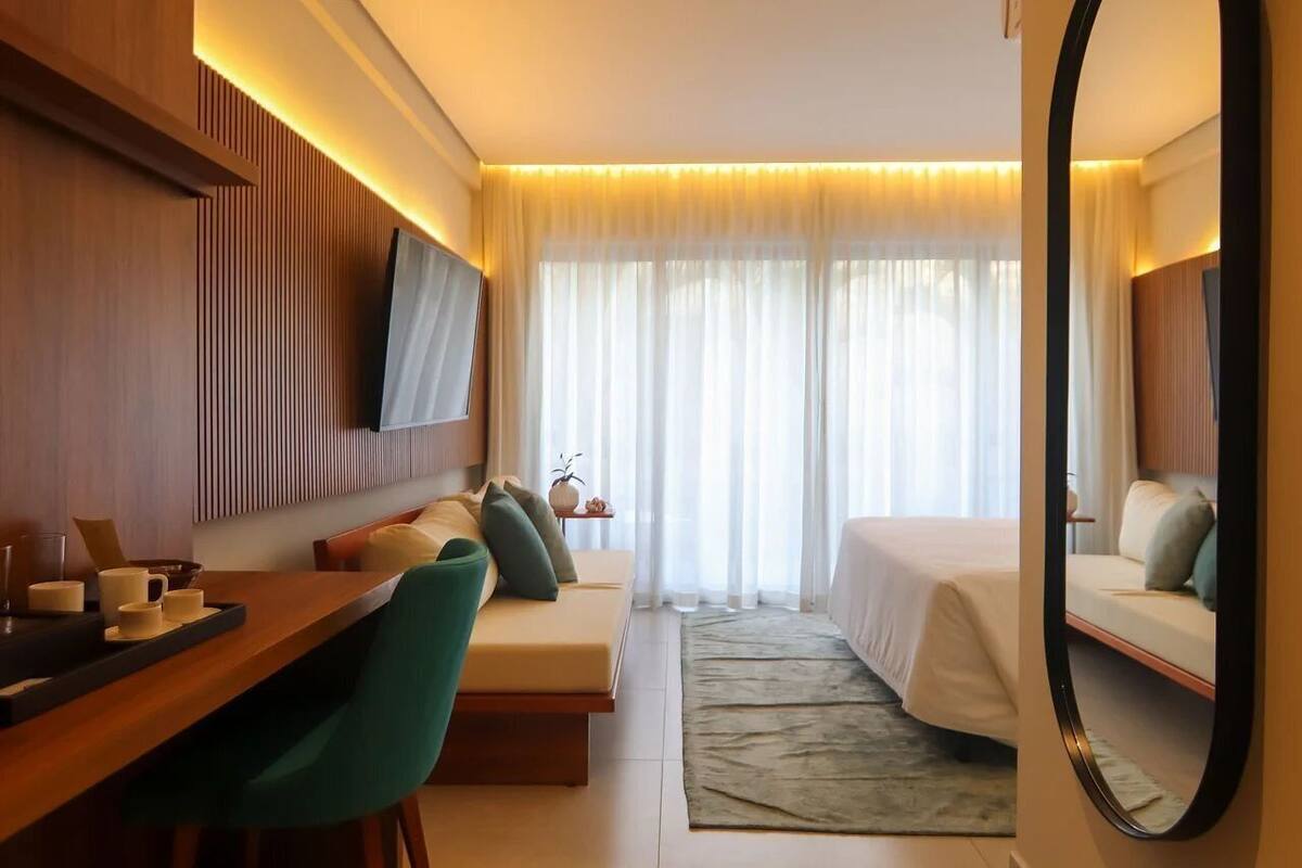 A hotel room with a bed, a sofa, a desk, a mirror, and a TV.