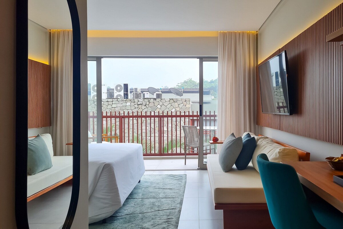 Ein Hotelzimmer mit Balkon, einem Bett, einer Couch, einem Fernseher und einer Essecke.