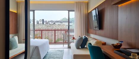 A hotel room with a balcony, a bed, a sofa, a TV, and a dining area.