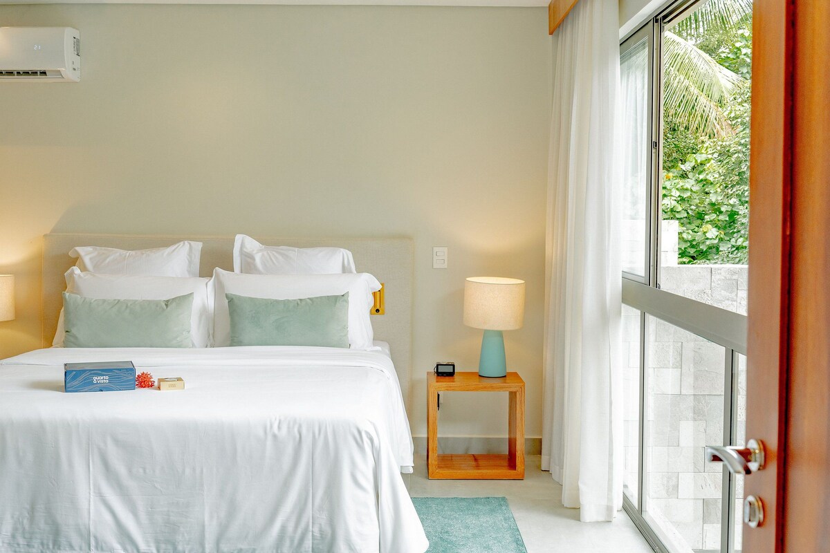 Habitación de hotel con cama, mesitas de noche, ventana con cortinas y vistas a zonas verdes.