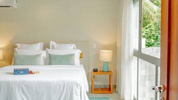 Quarto de hotel com cama, mesas de cabeceira, janela com cortinas e vista para o verde lá fora.