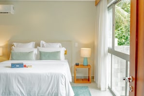 A hotel room with a bed, bedside tables, a window with curtains, and a view of greenery outside.