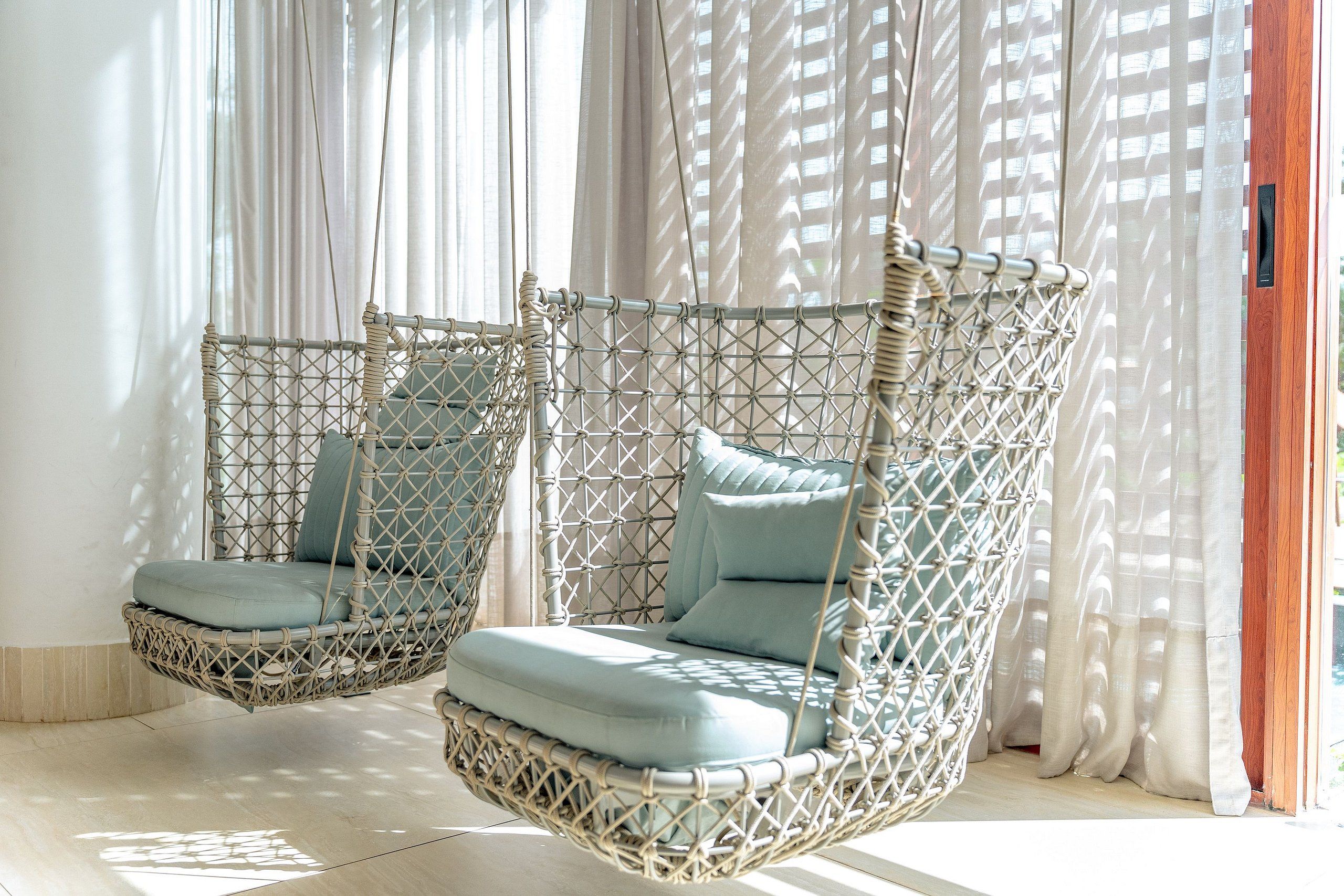 Two wicker swing chairs with cushions, positioned near a window with sheer curtains.