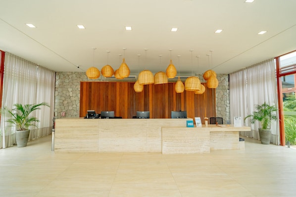 Un mostrador de recepción con un fondo de pared de piedra, múltiples monitores de computadora y lámparas colgantes de mimbre.