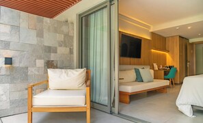 Ein modernes Hotelzimmer mit einer Steinwand, einem Holzsessel, einer Couch mit Kissen, einem Bett und einem an der Wand befestigten Fernseher.