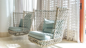Dos sillones colgantes de mimbre con cojines, ubicados cerca de una ventana con cortinas de encaje.
