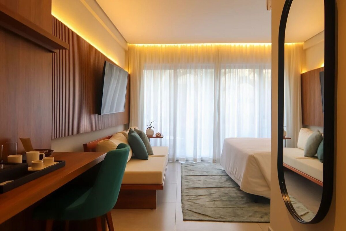 Une chambre d’hôtel avec un lit, un canapé, un bureau, un miroir et une télévision.