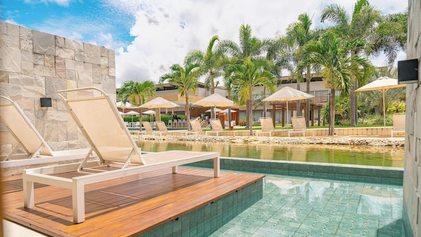 Un área de piscina con sillones reclinables, una terraza de madera y palmeras.