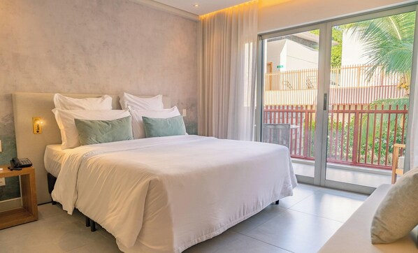 Une chambre d’hôtel avec un grand lit, une table de chevet avec un téléphone et une vue sur un balcon doté d’une balustrade.