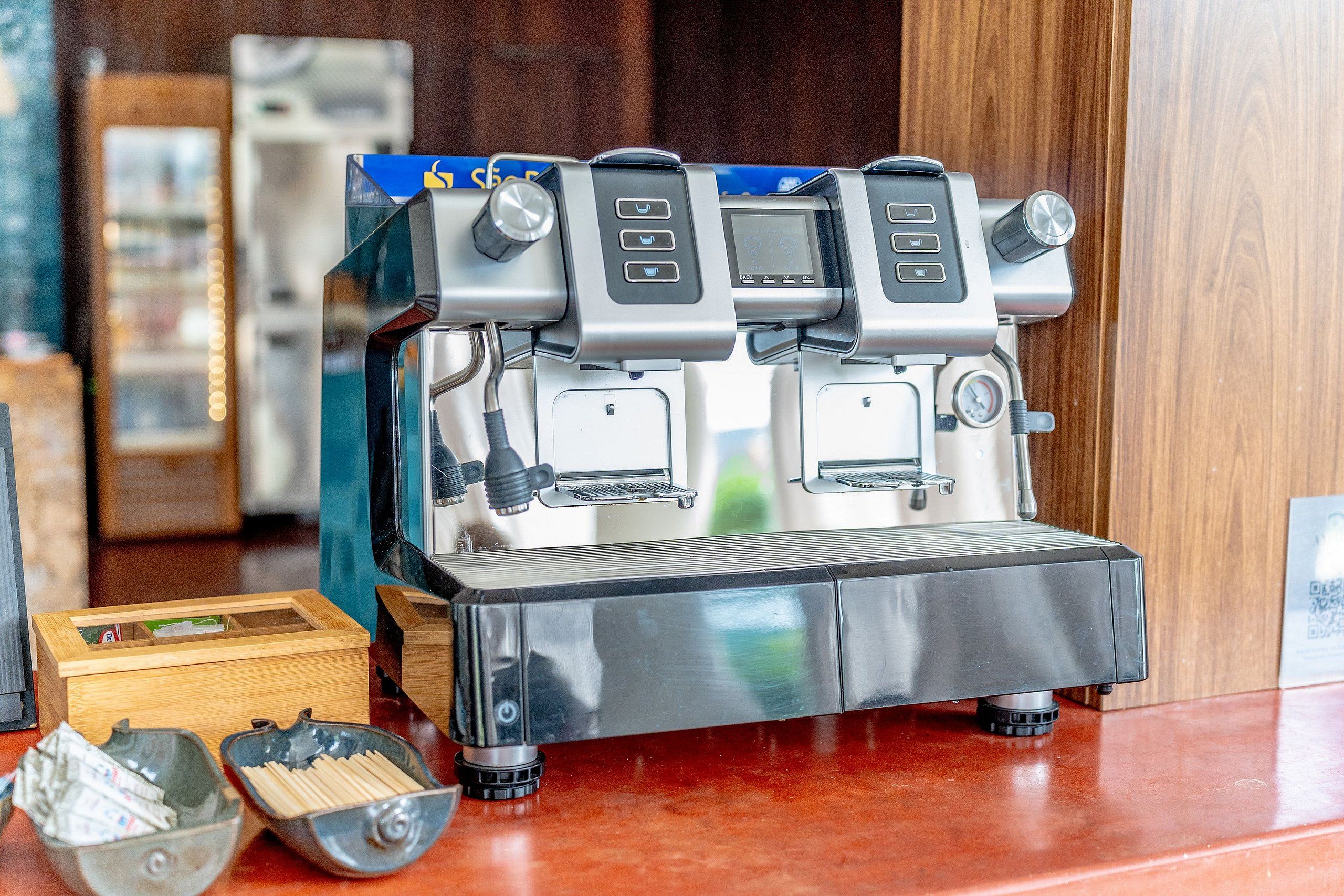 Una cafetera con pantalla digital y varios botones, una caja de madera y un recipiente metálico sobre una encimera.