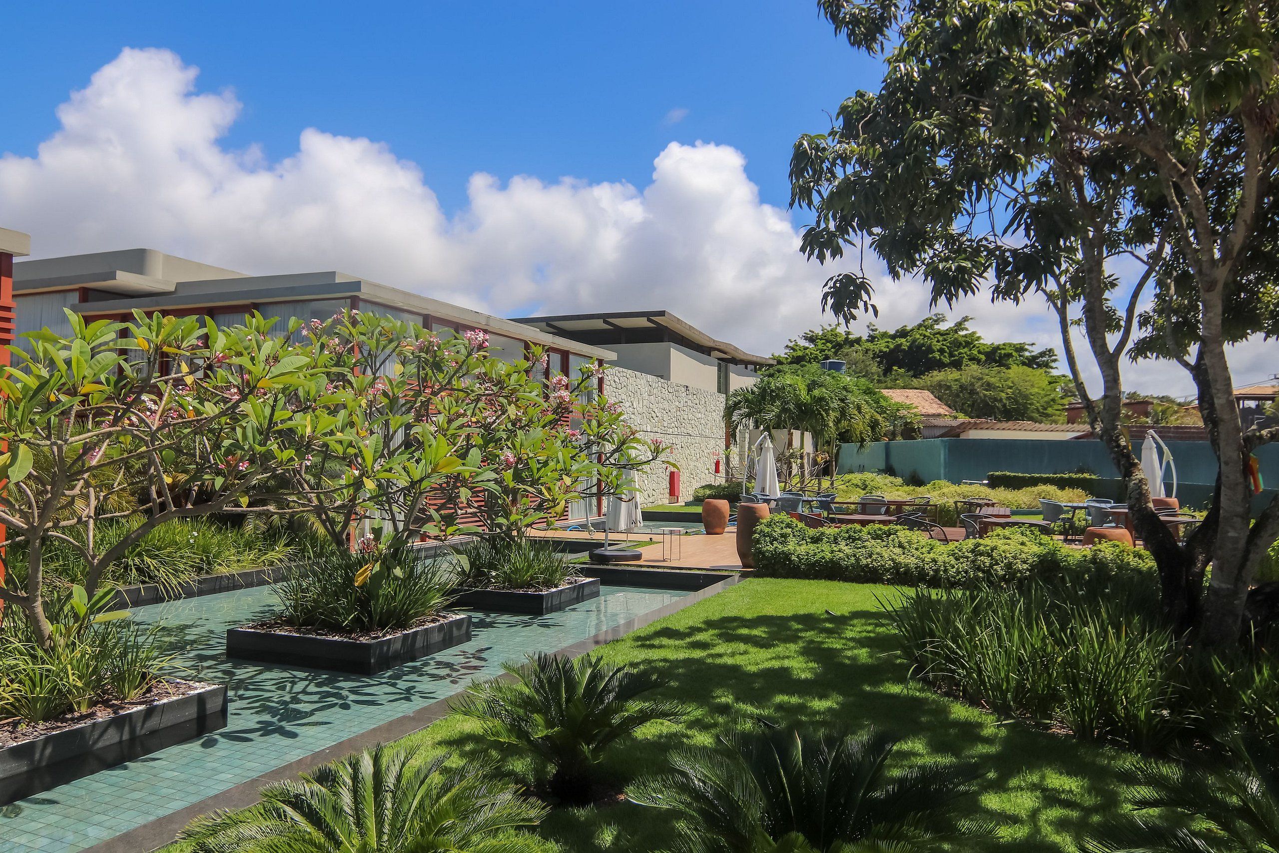 A modern hotel with a swimming pool, lush greenery, and outdoor seating areas.