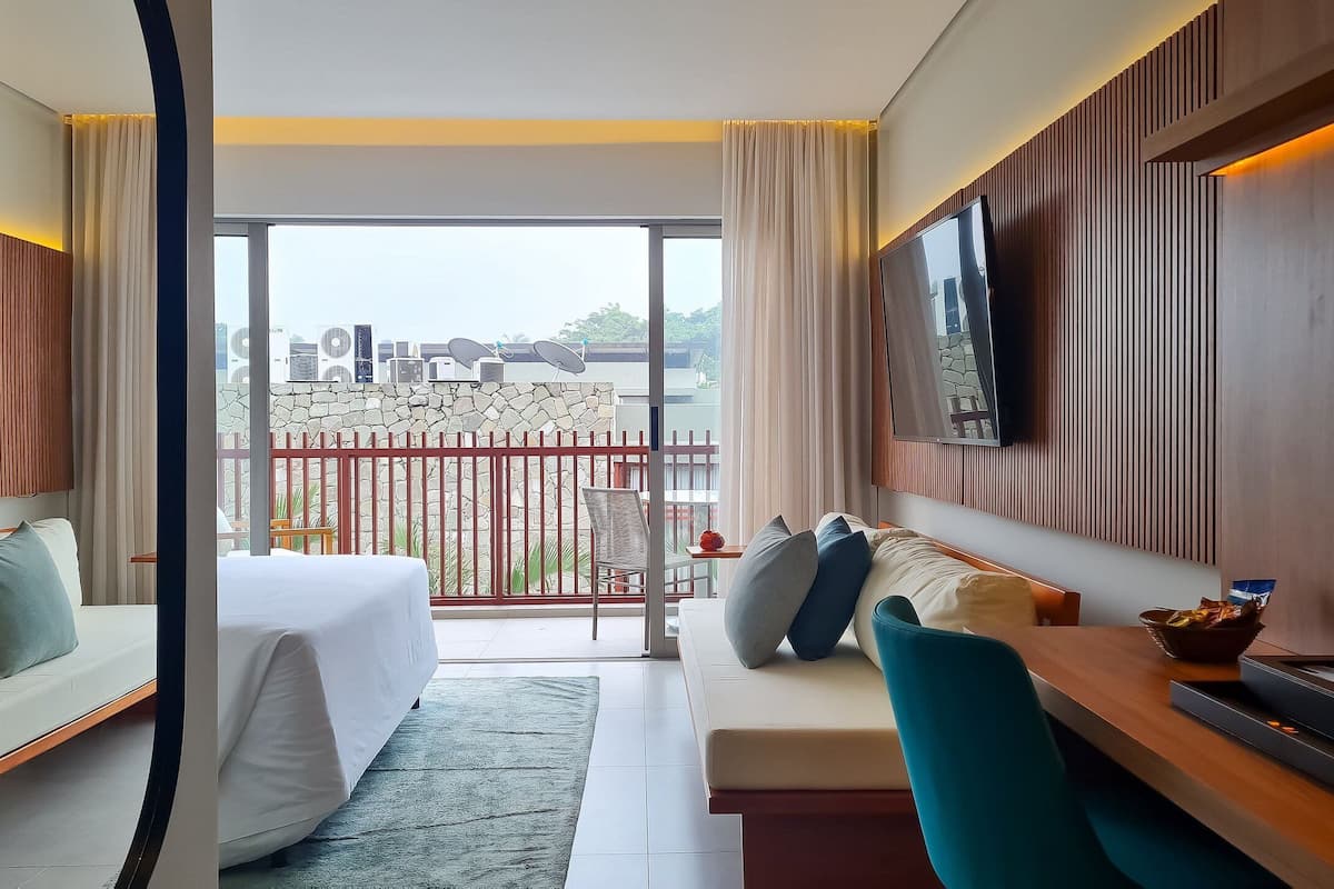 A hotel room with a balcony, a bed, a sofa, a TV, and a dining area.