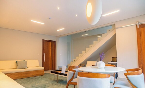 A modern living room with a sofa, a dining table with chairs, and a staircase. - Île de Pipa - Ma Plage Hotel (Tibau do Sul)