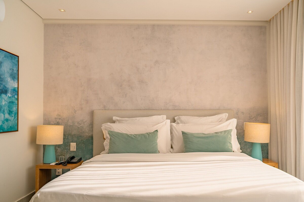 Une chambre d’hôtel avec un grand lit, deux tables de chevet avec des lampes, un tableau au mur et une fenêtre avec des rideaux.