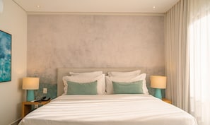 Habitación de hotel con una cama grande, dos mesitas de noche con lámparas, un cuadro en la pared y una ventana con cortinas.