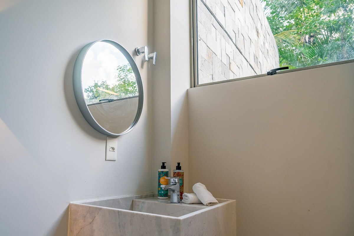 Une salle de bain avec un lavabo en marbre, un miroir rond et deux flacons de produits de toilette.