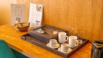 A hotel reception area with a wooden counter, a menu board, a basket of snacks, a tray with coffee cups and a teapot, and a sign with service options.