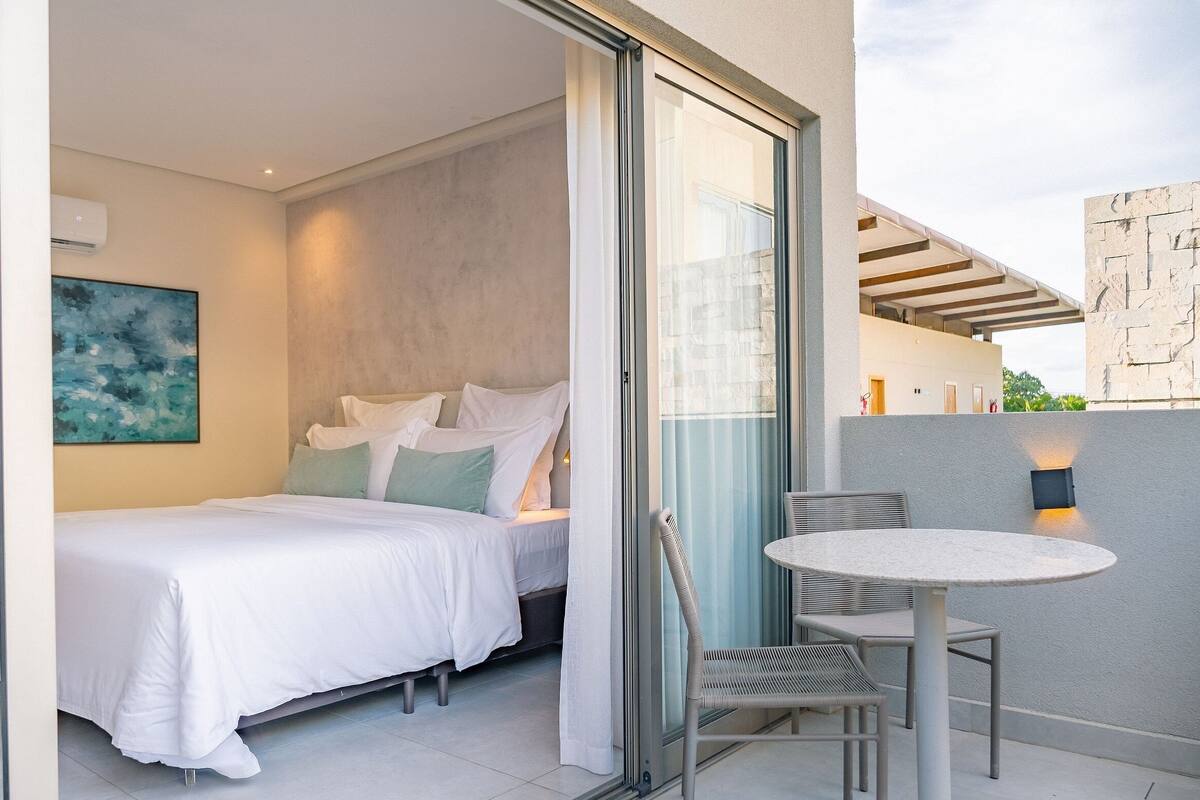 A bedroom with a bed, a glass door leading to a balcony, and a painting on the wall.