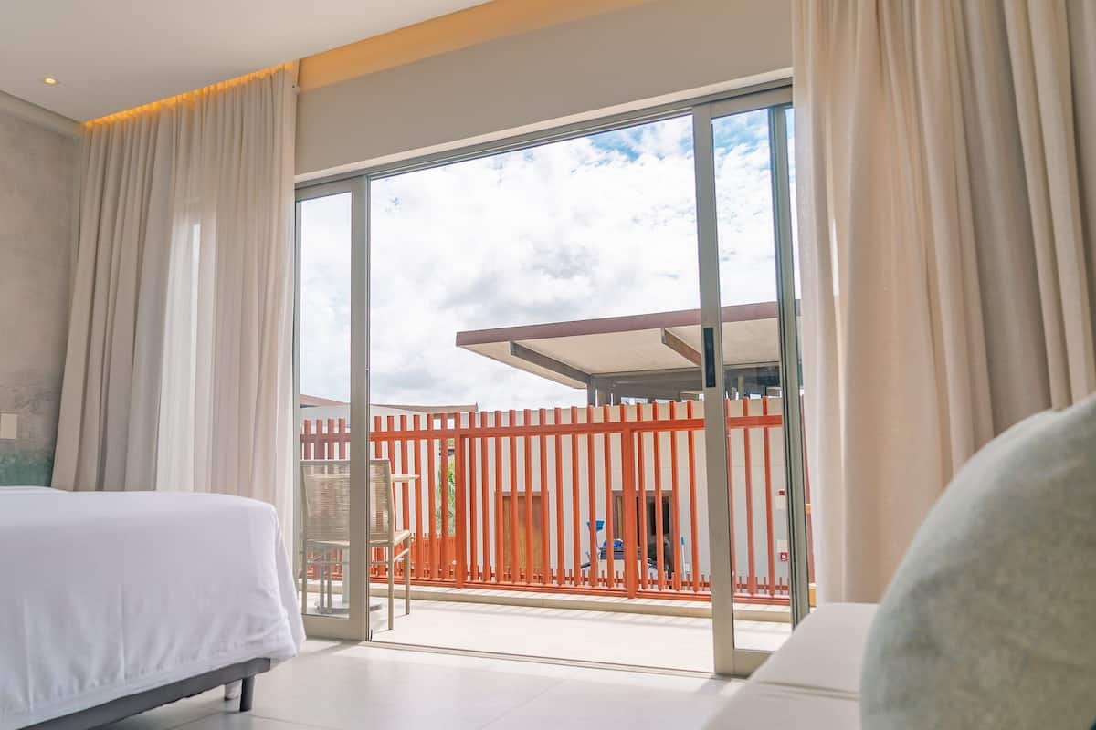A hotel room with a bed, a balcony with a view, and a sliding glass door.