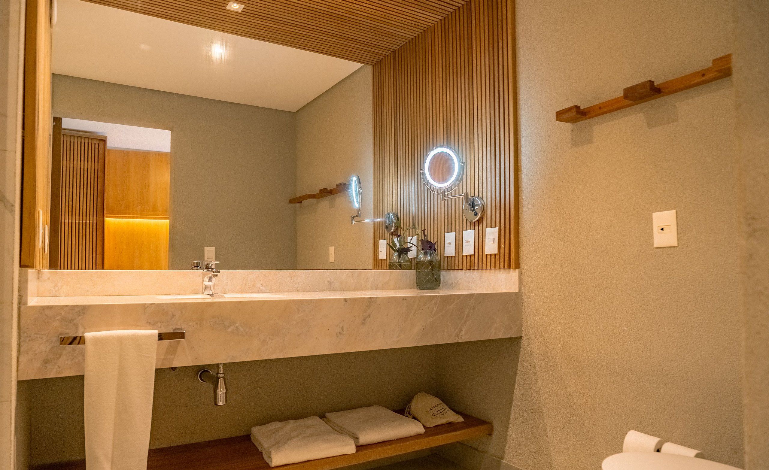 A bathroom with a large mirror, wooden panel wall, and a towel rack.