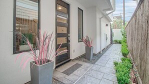 Een modern exterieur met een strakke, witte gevel, een donker houten deur en twee grote ramen.