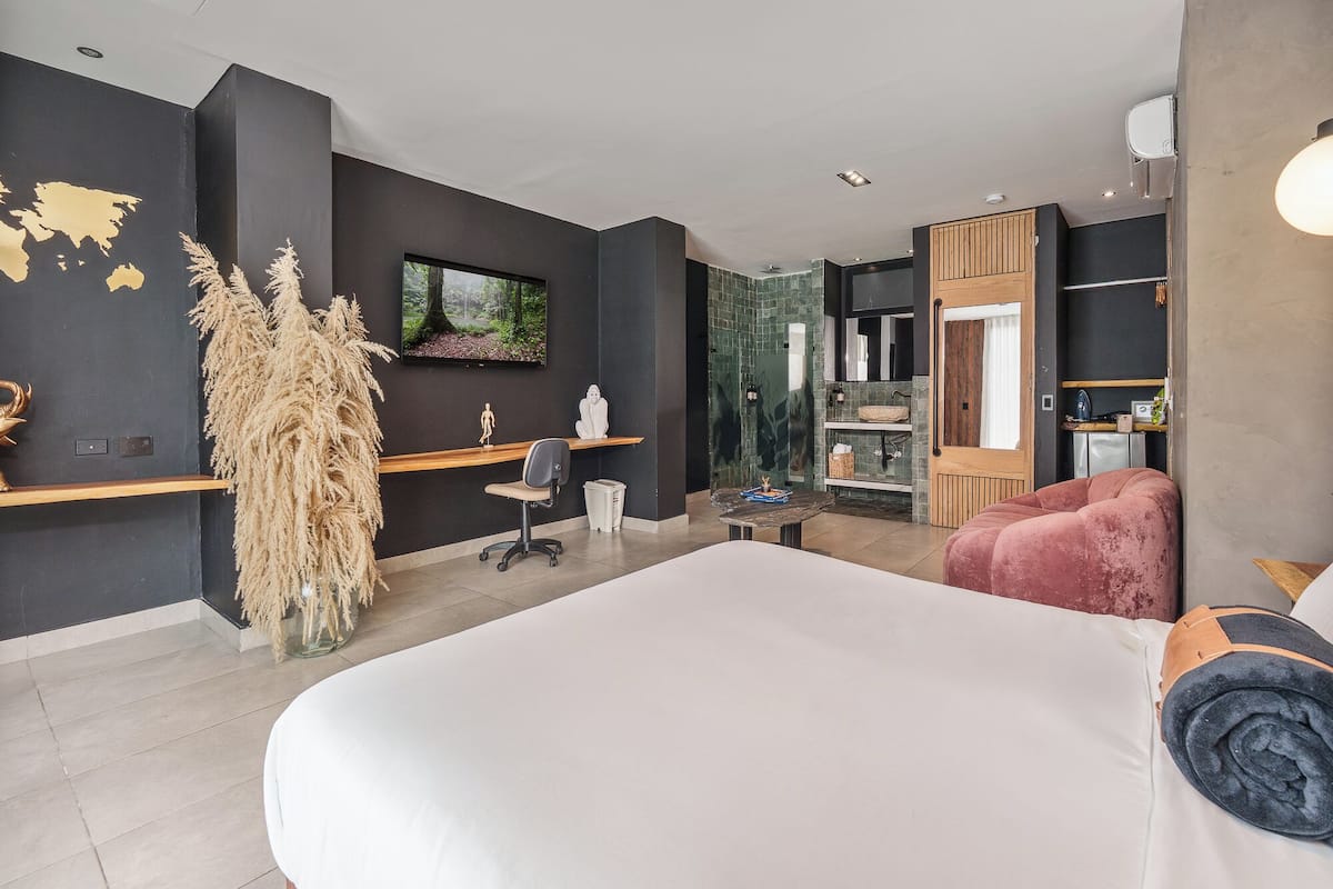 A modern hotel room with a large bed, a desk, a chair, a TV, and a wardrobe.
