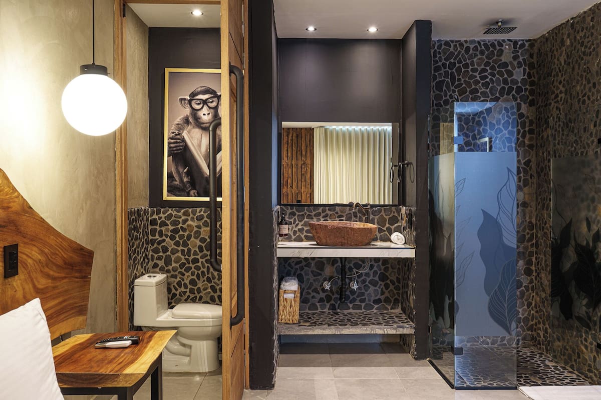 A bathroom with a stone wall, a wooden vanity, a large mirror, and a toilet.