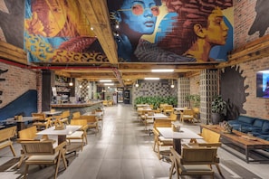 Un restaurante con mesas y sillas de madera, una zona de bar y un mural en la pared.