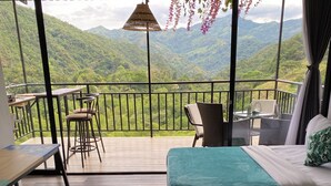 A balcony with a wooden floor, two beds with teal bedding, a hanging light fixture, and a view of green mountains. - Amari:cabaña Garzas, di Vega Cundinamarca. Balcón,terraza,jacuzzi (La Vega)