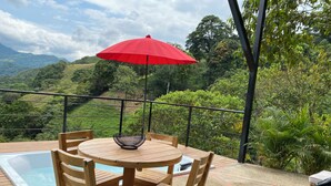 A wooden table with four chairs and a red umbrella on a balcony overlooking a lush green landscape with a pool. - Amari:cabaña Garzas, di Vega Cundinamarca. Balcón,terraza,jacuzzi (La Vega)