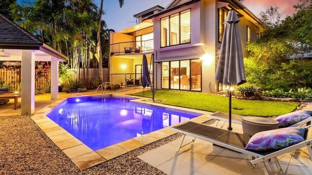 Ein zweistöckiges Haus mit Swimmingpool, Sitzgelegenheiten im Freien und einem gut beleuchteten Garten.