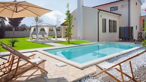 Una piscina con solarium in pietra, un gazebo e una zona salotto coperta.