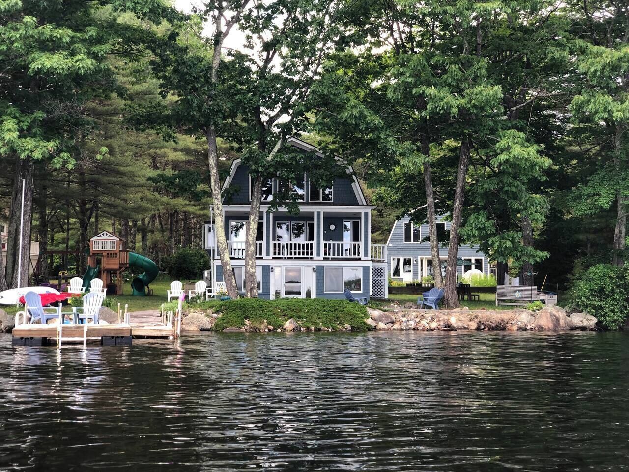 Una cabaña junto al lago con muelle, rodeada de árboles y un parque infantil.