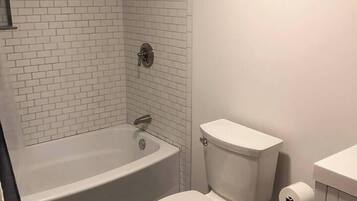 Un baño con una bañera blanca, inodoro y zona de ducha.
