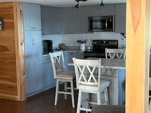 Une cuisine avec des meubles de couleur bleu clair, un four à micro-ondes, une cuisinière et deux chaises en bois.