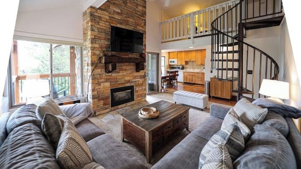A spacious living room with a stone fireplace, a large sectional sofa, and a kitchen in the background.