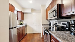 A kitchen with wooden cabinets, stainless steel appliances, granite countertops, and a white door.