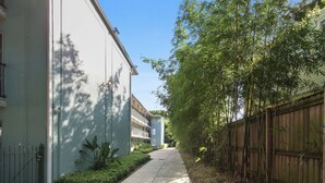 A narrow pathway flanked by a white building and a bamboo fence.